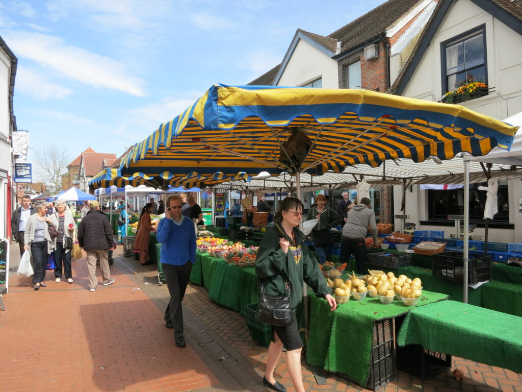 People walking past a fruit and vegetable stall.